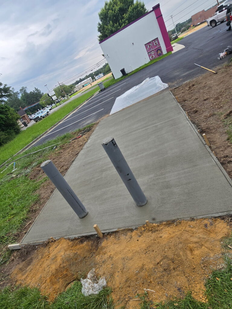New concrete pad at a commercial site with bollard pipe sleeves set before backfill